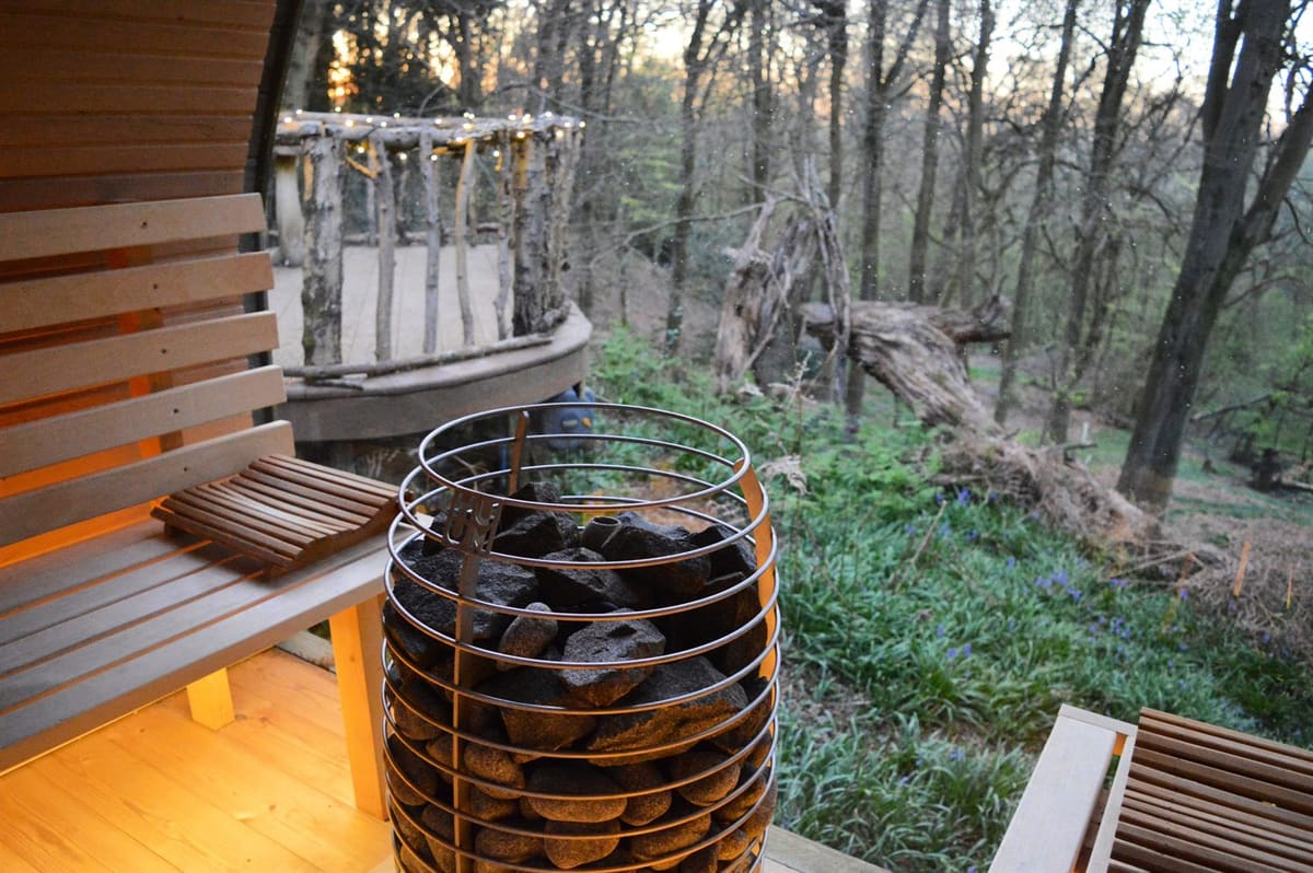 The view from inside the barrel sauna at dusk, out across a lantern-strung deck to darkening woodland