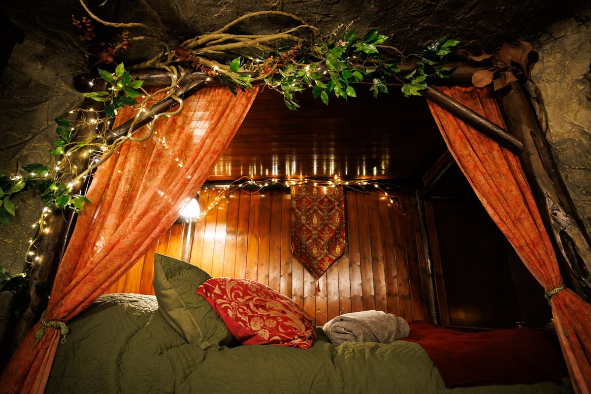 A canopied bed inside Faun's Hideaway, draped in fairy lights and garlands beneath a rock-carved ceiling